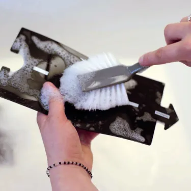 Nettoyage d’un coffret de routes nationales Waytoplay: une pièces noire avec mousse savonneuse et une brosse blanche est frottée.