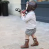 Jeune garçon portant un casque de pilote, debout sur un pavage, tenant une voiture de course miniature Racing Car Silver Baghera gris métal N°3.