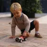Petit garçon jouant avec une voiture miniature rouge et blanche sur un sol en pavés.