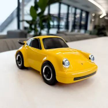 Voiture jouet Porsche 911 jaune sur socle clair, design miniature avec roues noires et phares détaillés.