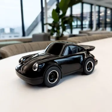 Voiture jouet Porsche 911 Noire de Baghera, petit modèle noir brillant sur table blanche en intérieur.