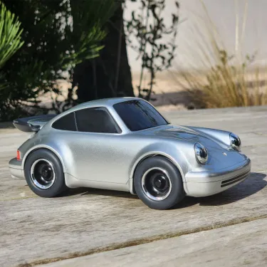 Voiture-jouet Porsche 911 argentée de marque Baghera, miniature Racing Car, vue de profil sur plancher bois en extérieur.