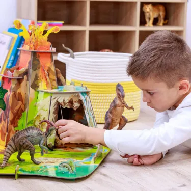 Jeu de dinosaures en relief avec un garçon jouant près d’un décor 3D coloré. Figurines, rochers, têtes d’animaux préhistoriques. La terre des dinosaures PAPO 60600.