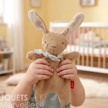 Doudou lapin marron SIGIKID 31268 en tissu éponge, enfant tenant la peluche avec un foulard, chambre de bébé en arrière-plan.