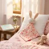 Doudou lapin SIGIKID 31274 en tissu rose à fleurs, posé sur un oreiller, lit pastel avec peluche et livre dans une chambre cozy.