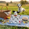 Doudou chien dalmatien SIGIKID 43594 sur une couverture à carreaux lors d’un pique-nique en plein air, avec panier, fruits et chapeau.