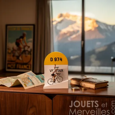 Borne kilométrique colorée D974 « Ventoux » avec petit cycliste miniature sur socle, disposée devant sur une table avec atlas et livre.
