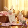 Doudou lapin blanc SIGIKID 31273 en tissu éponge, pose décorative avec lapin réel en arrière-plan, panier en osier et petit arrosoir sur une nappe rose fleuries.