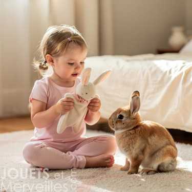 Petite fille en tenue rose jouant avec un doudou lapin blanc en tissu éponge, devant un lapin nain.