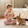 Petite fille en tenue rose jouant avec un doudou lapin blanc en tissu éponge, devant un lapin nain.