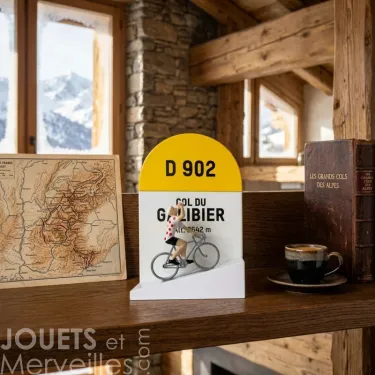Borne kilométrique jaune D 902 « Gol du Galibier » avec petit cycliste miniature sur bicyclette devant un livre et une carte ancienne.