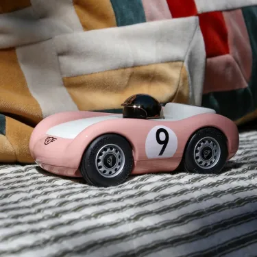Voiture de course Viglietta Playforever Dottie, véhicule design vintage rose pâle avec numéro 9 sur le flanc et pilote avec casque bronze.