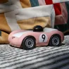 Voiture de course Viglietta Playforever Dottie, véhicule design vintage rose pâle avec numéro 9 sur le flanc et pilote avec casque bronze.