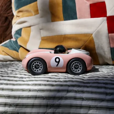 Voiture de course Viglietta Playforever Dottie, véhicule design vintage rose pâle avec numéro 9 sur le flanc et pilote avec casque bronze. Vue de profil.