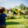 Petit planeur jaune DJECO 2100 "Fire Jet" pris en vol en plein jardin, enfant en arrière-plan prêt qui le lance.