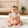 Doudou Miffy en crochet, poupée lapin rose pastel tenue par un bébé assis sur drap crème, serre-tête rose.