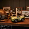 Voiture de course Viglietta Playforever Birdy vintage, modèle miniature vert et doré n°8, sur une étagère avec casques, trophée et photos noir et blanc.