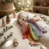 Doudou en coton bio « Nuage arc-en-ciel »: bébé tenant un hochet en forme de nuage tricoté et de linge multicolore et jouets en bois.