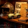 Voiture de course Viglietta Playforever Birdy vintage sur étagère, entourée d’un casque, livre ancien et trophée, ambiance bibliothèque vintage.