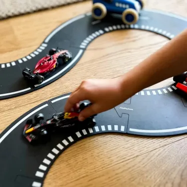 Circuit Grand Prix Waytoplay: coffret 24 pcs - enfant joue avec des voitures miniatures sur un circuit modulable noir et blanc posé sur une table en bois.