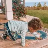 Enfant jouant avec un circuit de course sur une terrasse en bois, trainant une petite voiture sur le tracé du circuit. Jardin et mer à l’horizon.