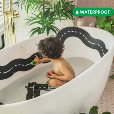 Enfant jouant dans une baignoire avec un circuit de route flexible Waytoplay en noir et blanc autour des bords, coffret Autoroute 24 pièces.