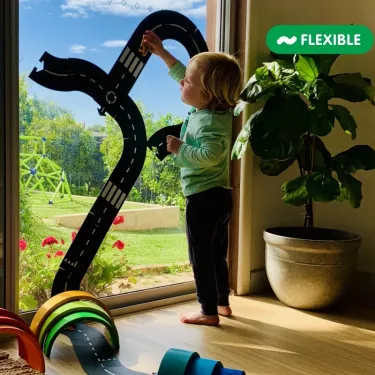 Jeu d’enfant avec le circuit de route flexible Waytoplay en coffret Autoroute 24 pcs, enfant près d’une porte-fenêtre en intérieur jouant sur la vitre.