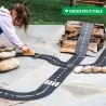 Circuit de route flexible Waytoplay, coffret Autoroute 24 pcs: enfant joue avec son circuit, bandes noires et lignes blanches, autour d’un petit tas de bois.
