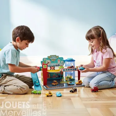 Deux enfants jouent avec un garage en bois Crazy Motors DJECO 5495, voitures miniatures et parking sur un plateau coloré posé au sol.