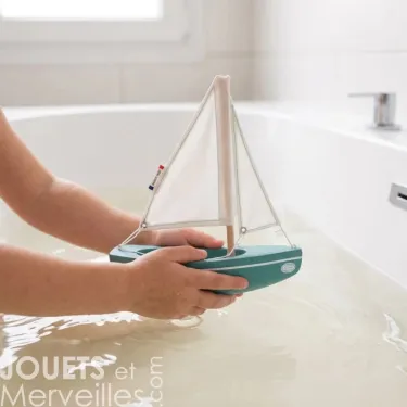 Sloop Tirot : petit voilier en bois blanc et bleu, mains d’enfant tenant le bateau flottant sur l’eau dans une baignoire.