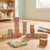 Cubes alphabet Uncle Goose formant des mots simples sur un sol en bois, avec livre enfant et petit coffre en bois à côté.
