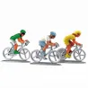 Trois figurines de cyclistes en course sur des étals, représentant une course à vélo avec des tenues colorées (vert, blanc/bleu et jaune).
