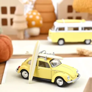Voiture miniature jaune pastel Volkswagen Coccinelle 1303 1973 NOREV 1/43 avec planche de surf à l’arrière, décor plage.