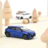 Renault Clio VI 2026 NOREV 1/64 en bleu iron, mini voiture Citadine sur une route légère, décorée de sapins en bois.