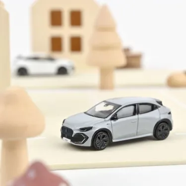 Renault Clio VI 2026 NOREV 1/64 – Gris Rafale, miniature voiture moderne sur socle beige avec décor urbain blurred.