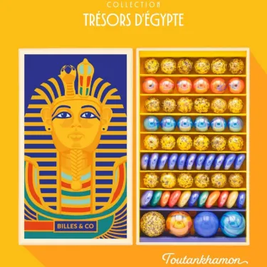 Grand coffret de billes "Toutankhamon" Billes & Co avec visage égyptien doré sur le couvercle et rangées de billes colorées dans le tiroir intérieur.