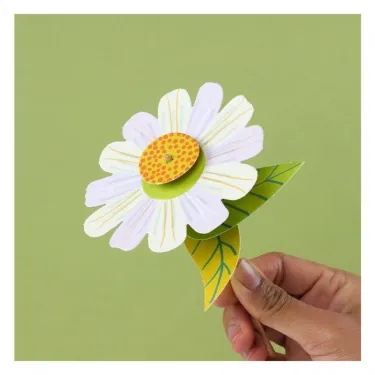 Fleur en papier blanche avec cœur jaune orange, tenue par une main, proposée dans le kit créatif “3 fleurs des champs à créer” Pirouette Cacahouète.