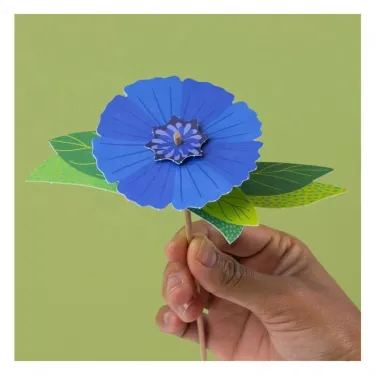 Petite main tenant un bâtonnet avec une grande fleur bleue en papier, kit créatif “3 fleurs des champs à créer” Pirouette Cacahouète.