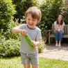 Enfant souriant faisant t/interagir un bâton de pluie en bois vert, jardin en arrière-plan et une femme assise sur un banc au fond.