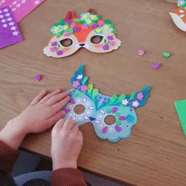 Masques mosaïques à décorer « Animaux de la forêt » DIY DJECO 7936 : enfants posant des motifs floraux et paillettes sur deux masques colorés.