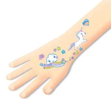 Tatouage temporaire licorne sur le poignet d’une main d’enfant, dessins arc-en-ciel et étoiles multicolores. Produit Tatouages Licornes DJECO 9575.