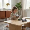 Une enfant joue avec des voitures miniatures Racing Car Silver, voiture Baghera gris métal N°3 - 480 sur une table en bois dans un salon lumineux.