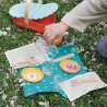 Mini pique-nique sur l’herbe avec vaisselle en couleur, assiettes jaunes et plats orange, verres décorés, couverts en bois, nappe turquoise et sac pique-nique Le pique-nique de Pâquerette, dînette DJECO 6527.