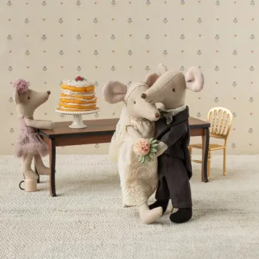 Couple de souris mariés dans leur coffret Maileg, les deux se serrent dans une étreinte près d’un gâteau nuptial sur un présentoir.