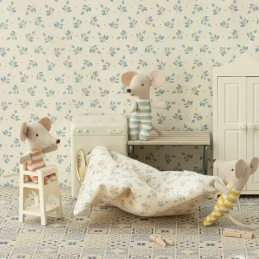 Chaise haute pour bébé souris Maileg, décor de chambre blanche crème avec souris en peluche, petite table, linge et linge de lit à motifs bleus.