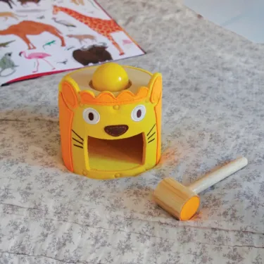 Petit tambour coloré en forme de lion avec ouverture pratique et maillet en bois posé à côté. Idéal jeu tactile SoftiTap DJECO.
