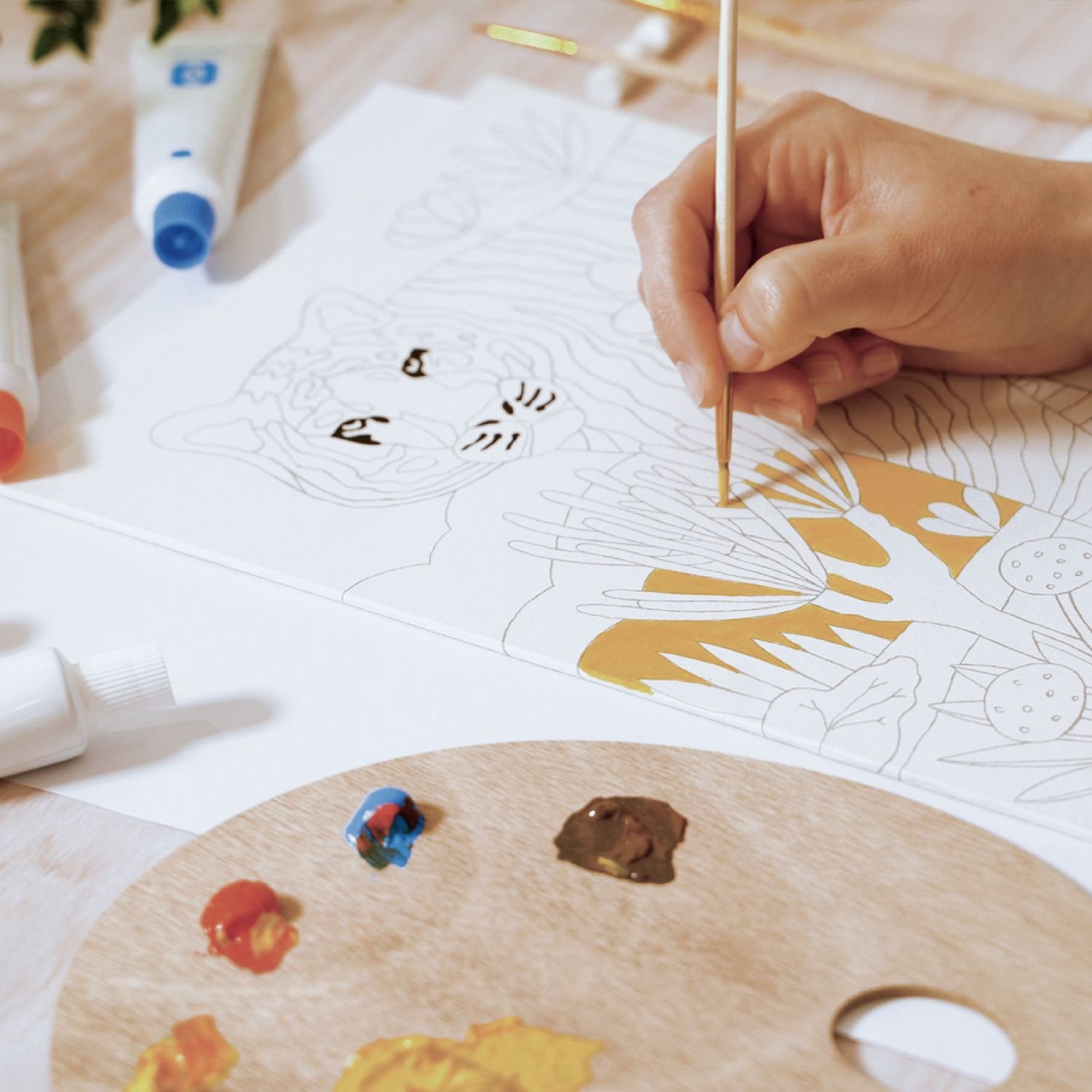 Adolescent dessinant avec un pinceau sur une feuille à colorier, palette et tubes de gouache à proximité, couleurs vives et beige au palette. Adolescent dessinant avec un pinceau sur une feuille à colorier, palette et tubes de gouache à proximité, couleurs vives et beige au palette.