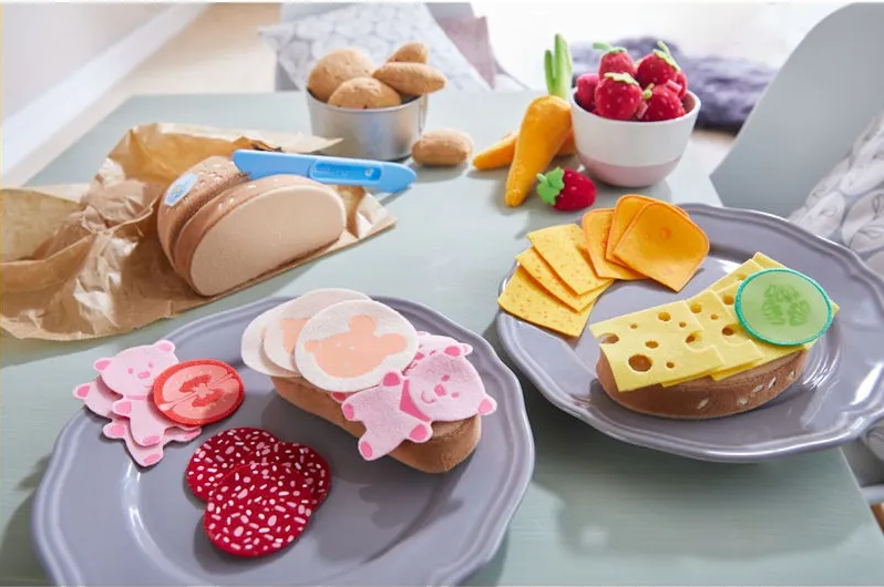 Assiette en jeu: tranches de pain miniature avec fromages et garnitures, fruits et biscuits colorés sur table, cadre décoratif pour enfants.