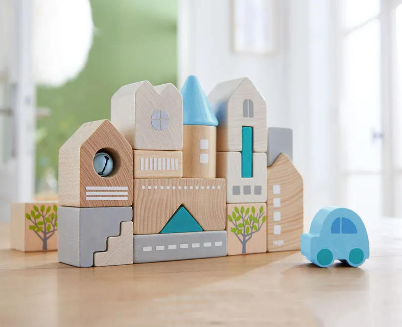 Blocs de construction en bois formant une mini-ville colorée avec maisons, rues et arbres, accompagnés d’une petite voiture bleue.