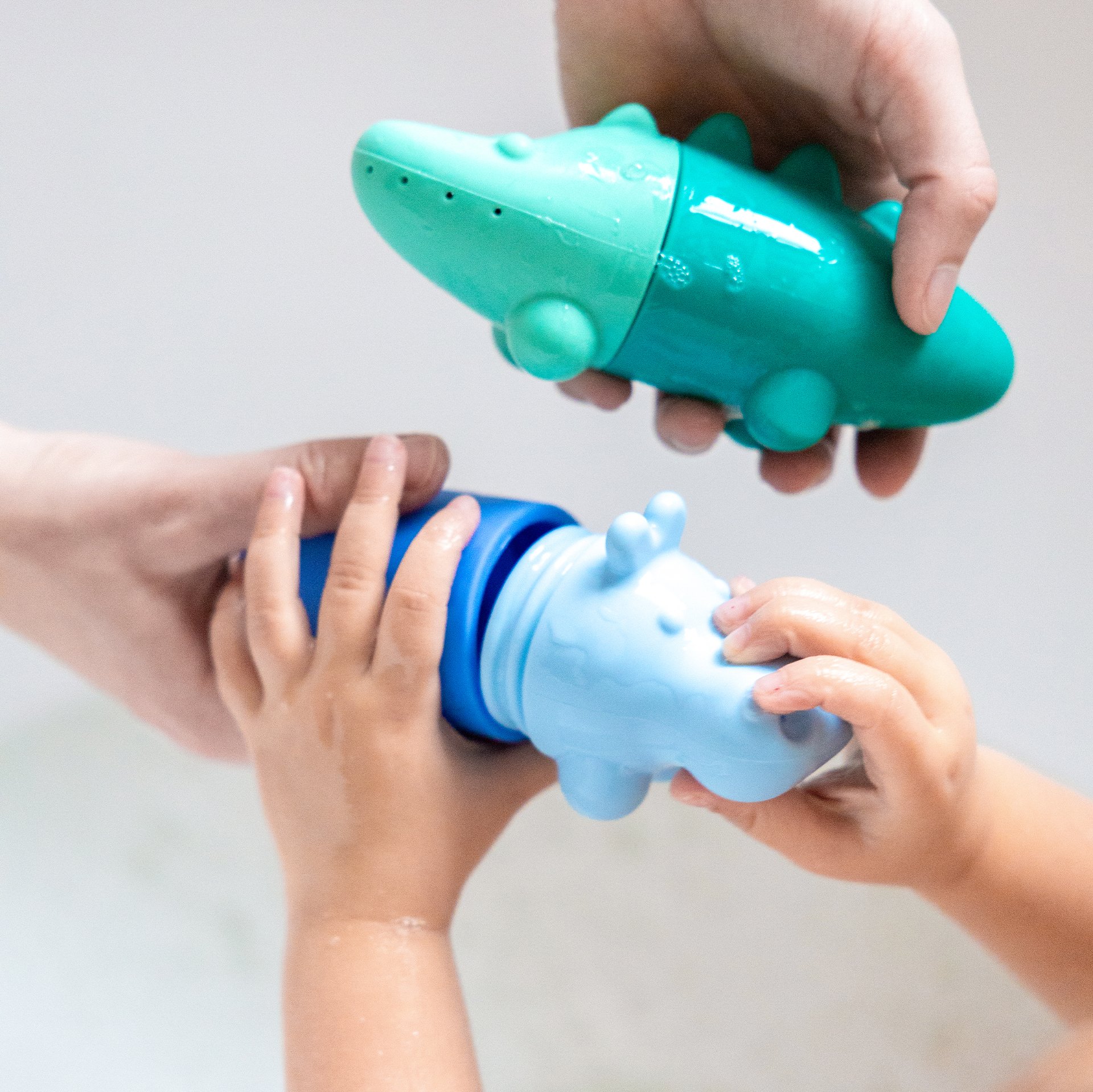 Deux enfants manipulent des jouets d’éveil en forme d’alligators colorés (turquoise et bleu) avec un petit capuchon centrifuge, sur fond clair.